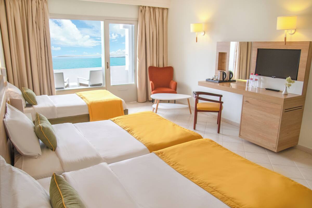 Een hotelkamer met twee bedden, een bureau, een stoel, een televisie en uitzicht op de oceaan.