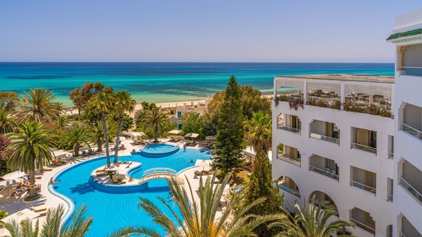 Un resort con una piscina grande, palmeras y vista al océano.