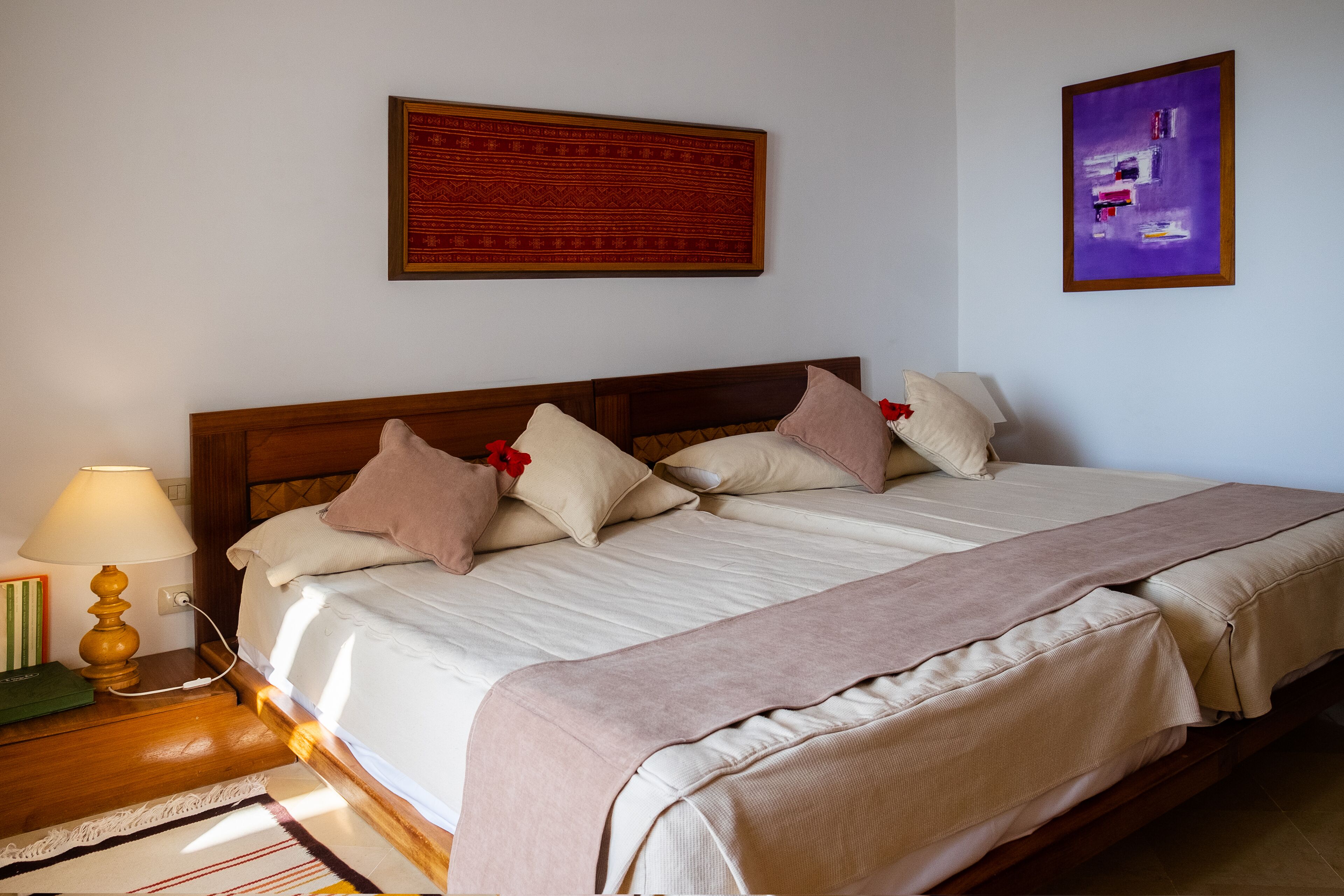 A neatly made bed with a wooden headboard, a bedside lamp, and a framed artwork above it.