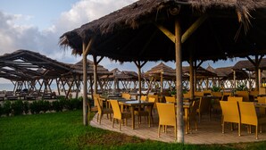 A beachside restaurant with outdoor seating under thatched umbrellas, wooden deck flooring, and a view of the sea. - The Orangers Beach Resort and Bungalows - All Inclusive (Hammamet)