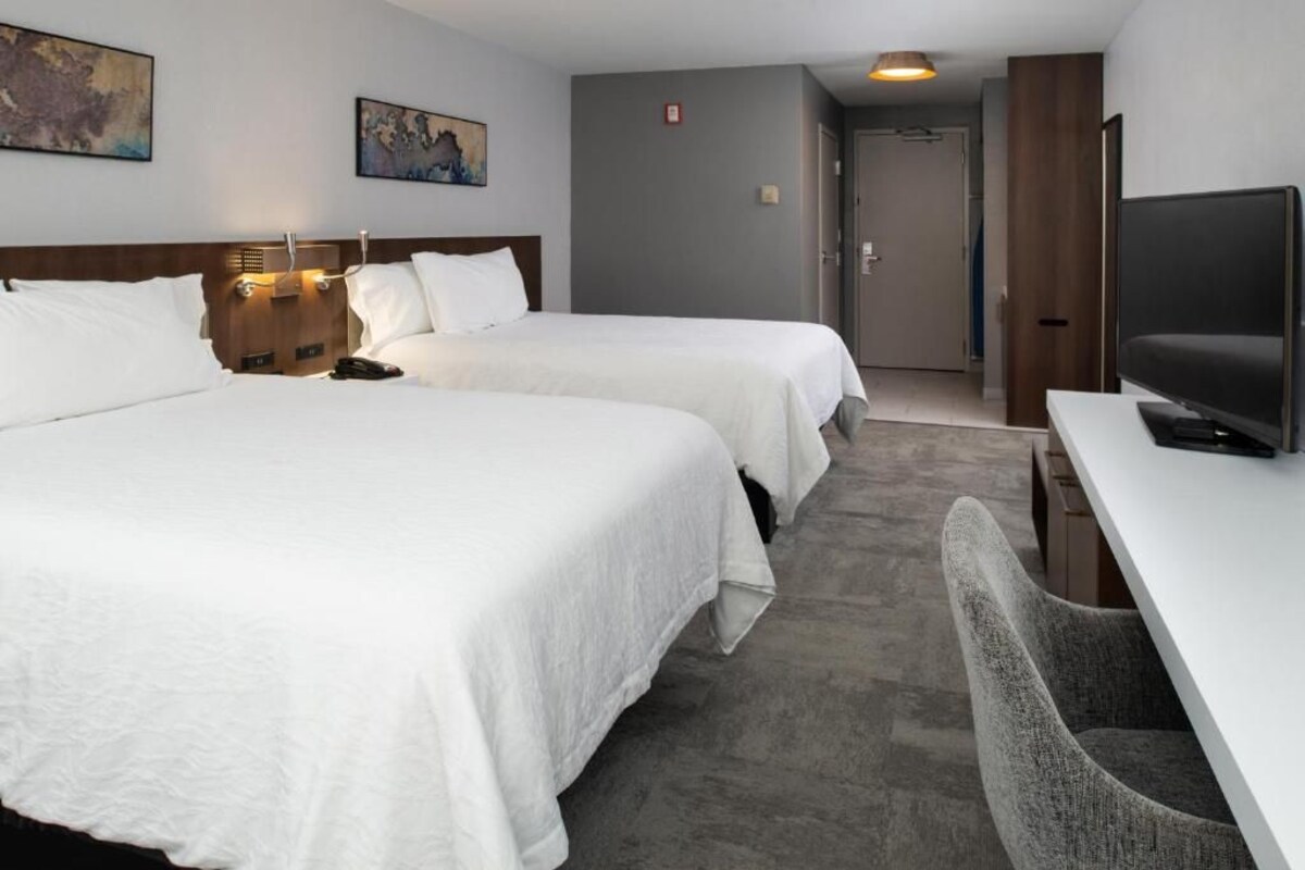 A hotel room with two beds, a desk, and a television.