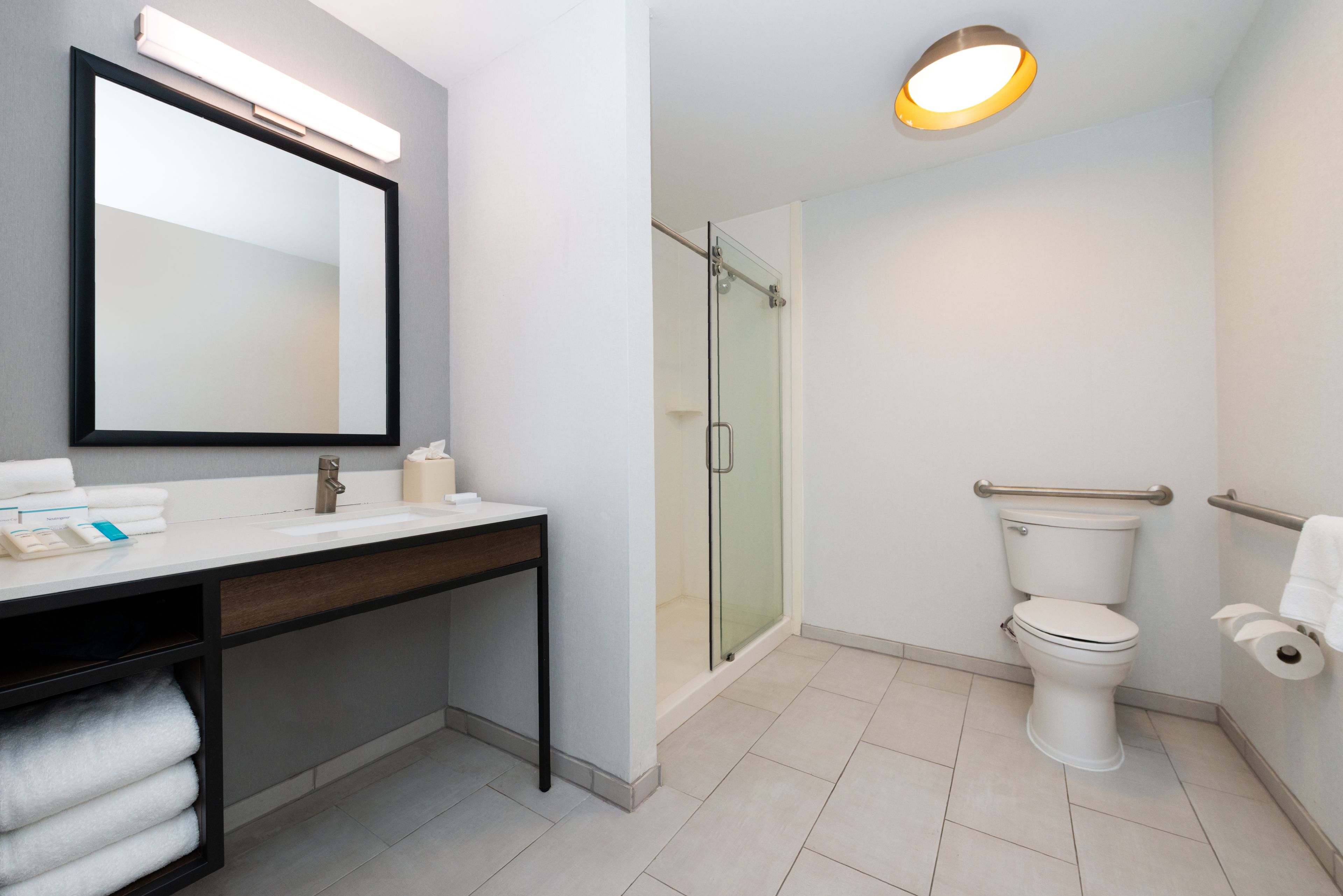 A modern bathroom with a glass-enclosed shower, a white toilet, and a vanity with a mirror and towel rack.