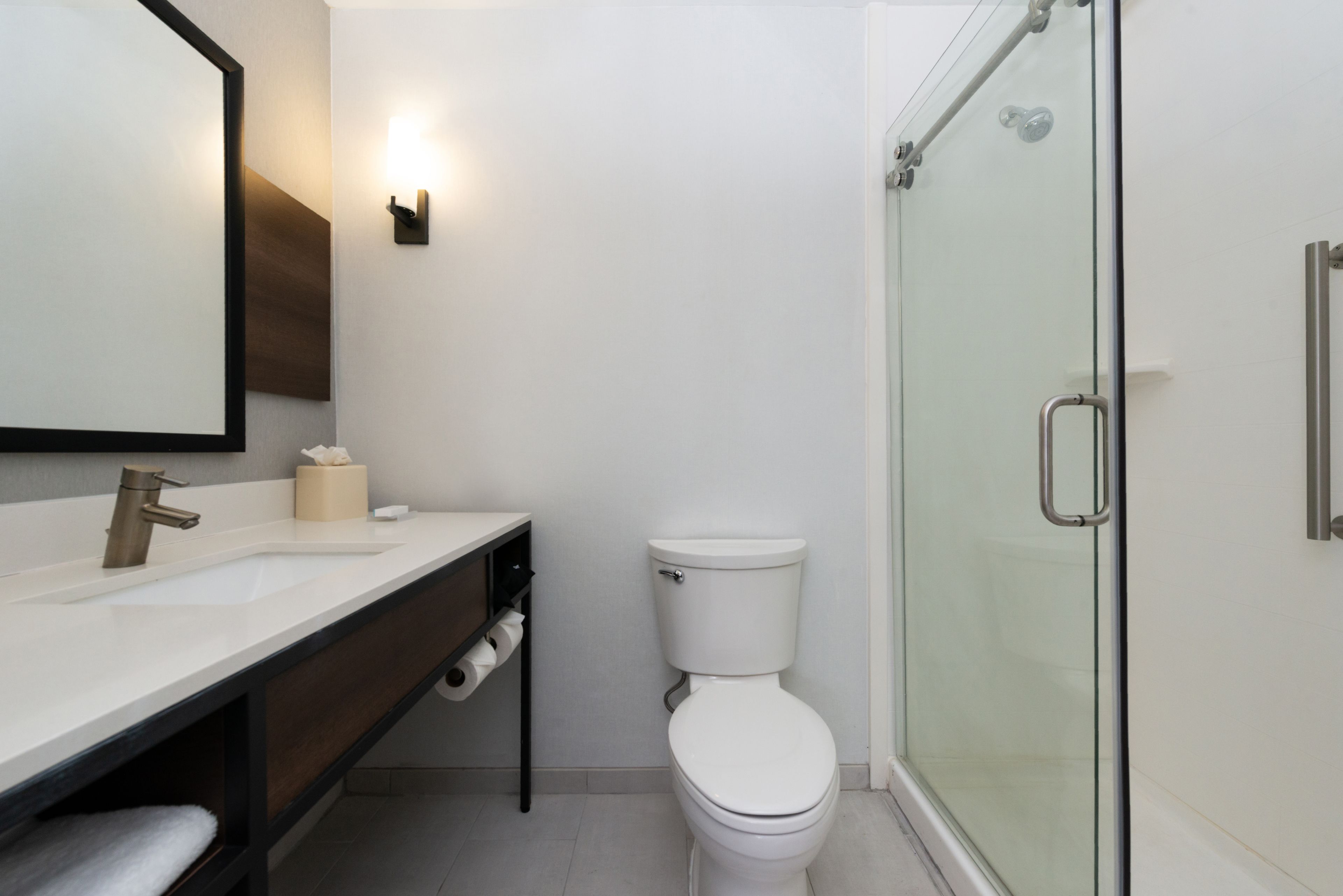 Une salle de bain moderne avec une douche à parois de verre, des toilettes blanches et un meuble-lavabo avec un miroir et un évier.