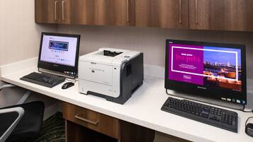 A hotel room desk with two monitors, a printer, and a keyboard.