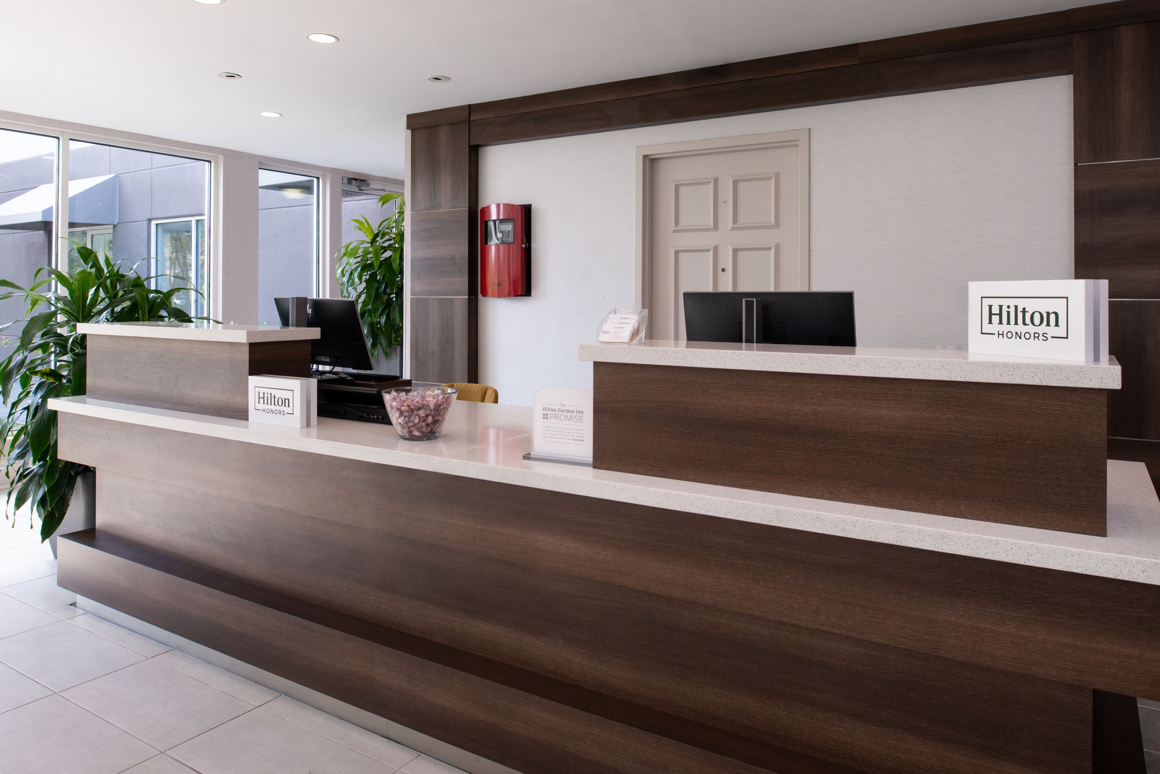 A modern hotel reception desk with a wooden finish, a digital screen, and a sign indicating Hilton Honors.