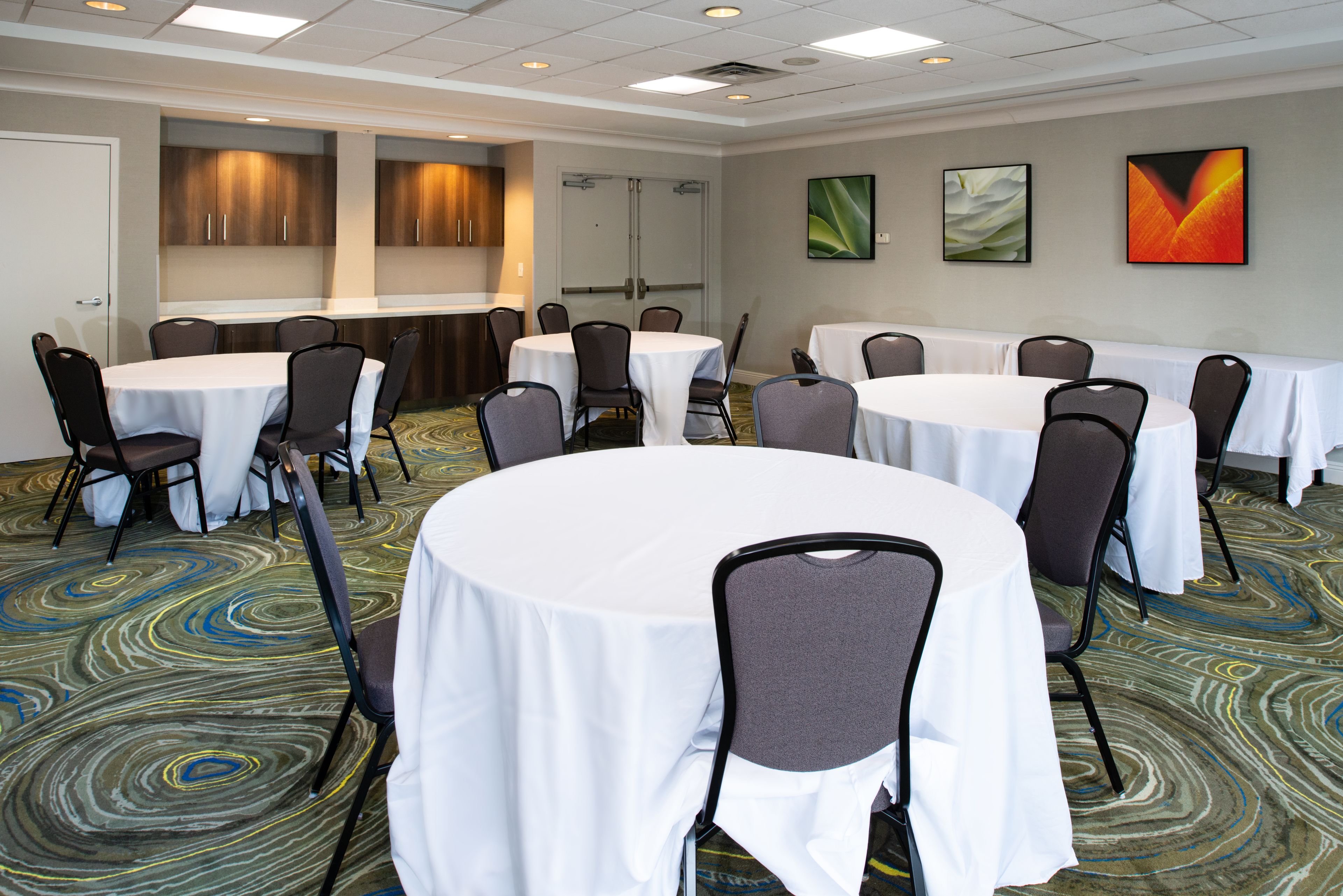 A conference room with round tables, chairs, and a carpeted floor.