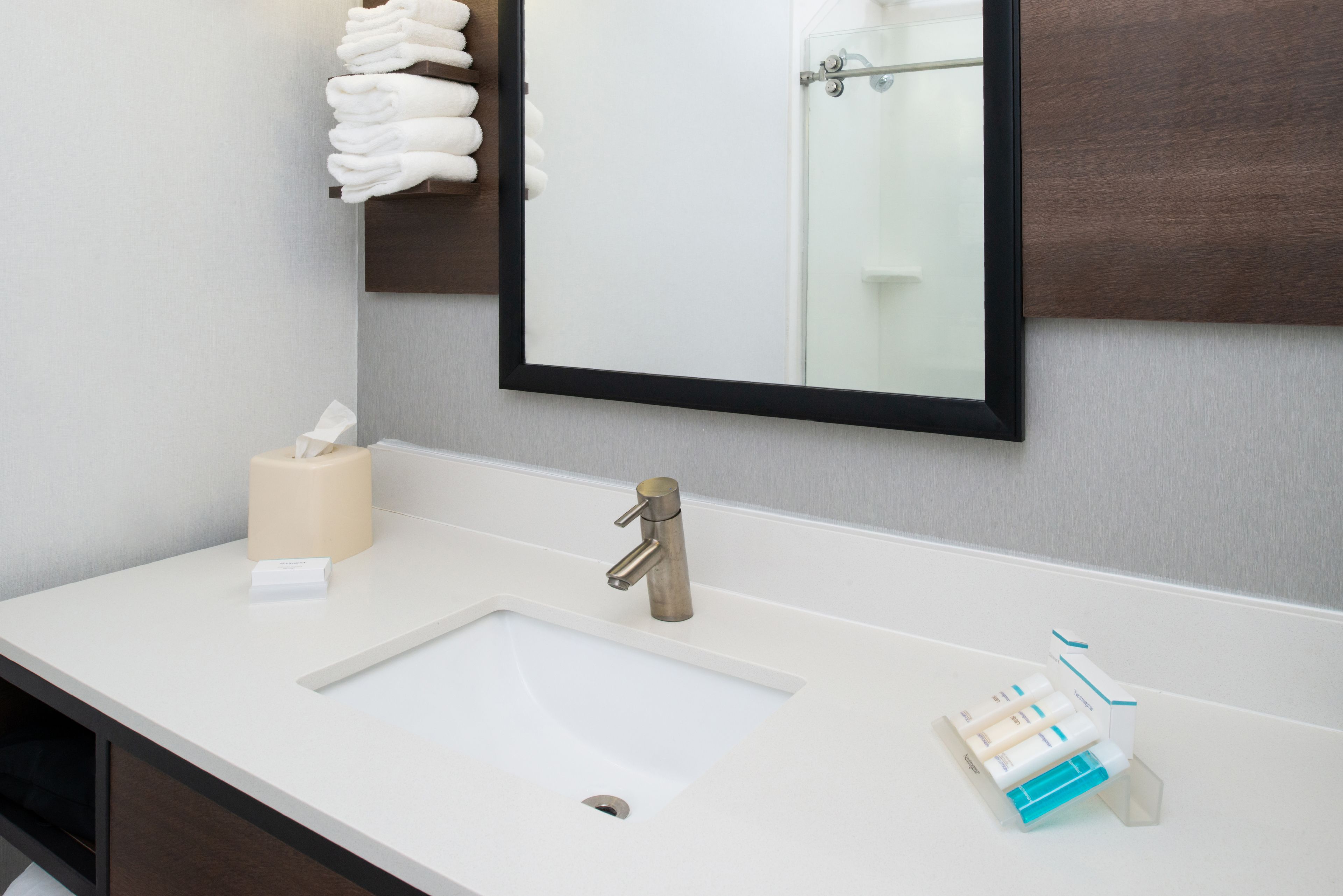 Un baño con lavamanos blanco, un espejo y un perchero para toallas.