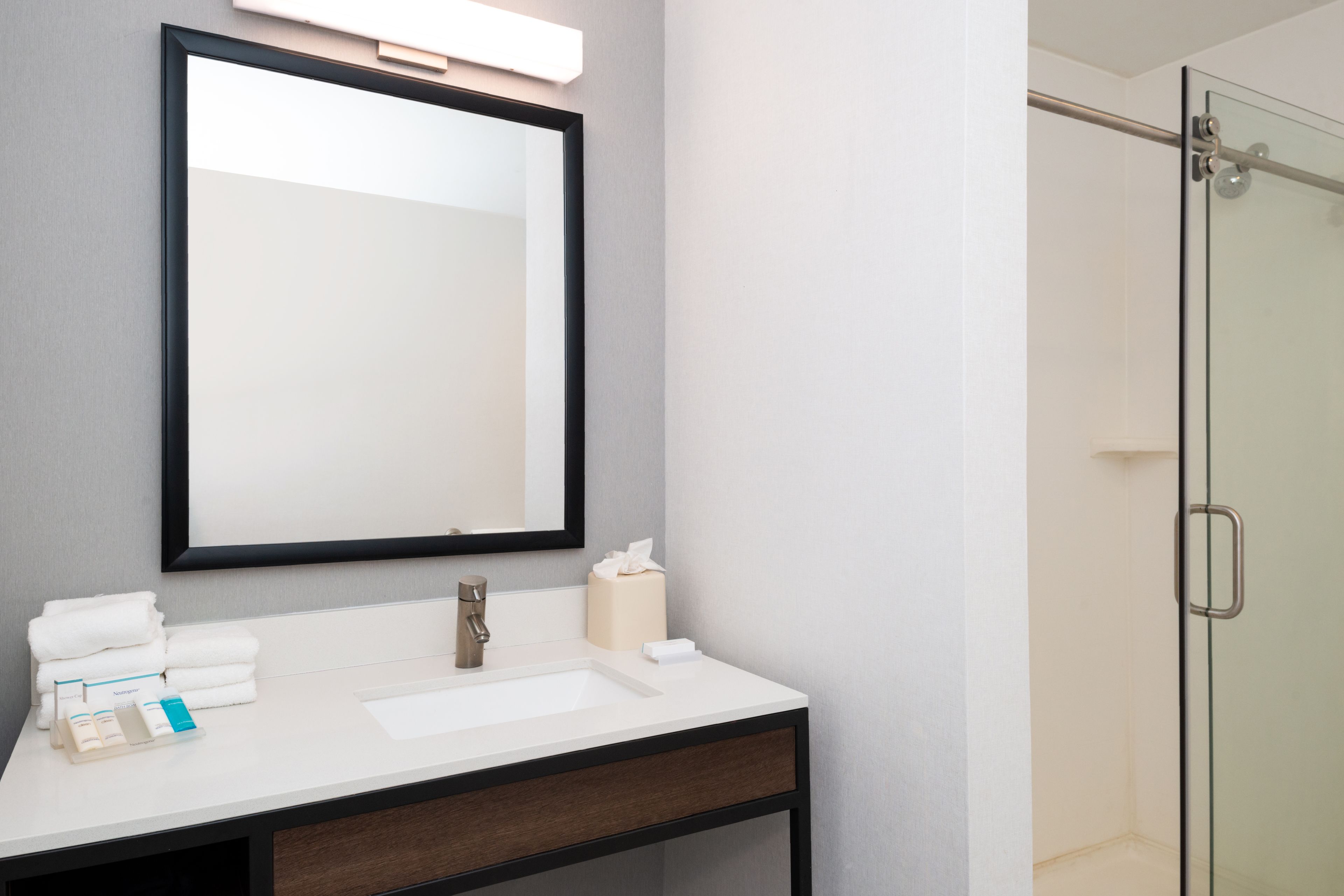 A bathroom with a white sink, a mirror, a towel rack, and a glass shower door.