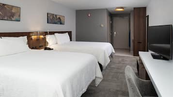 A hotel room with two beds, a desk, a television, and artwork on the walls.