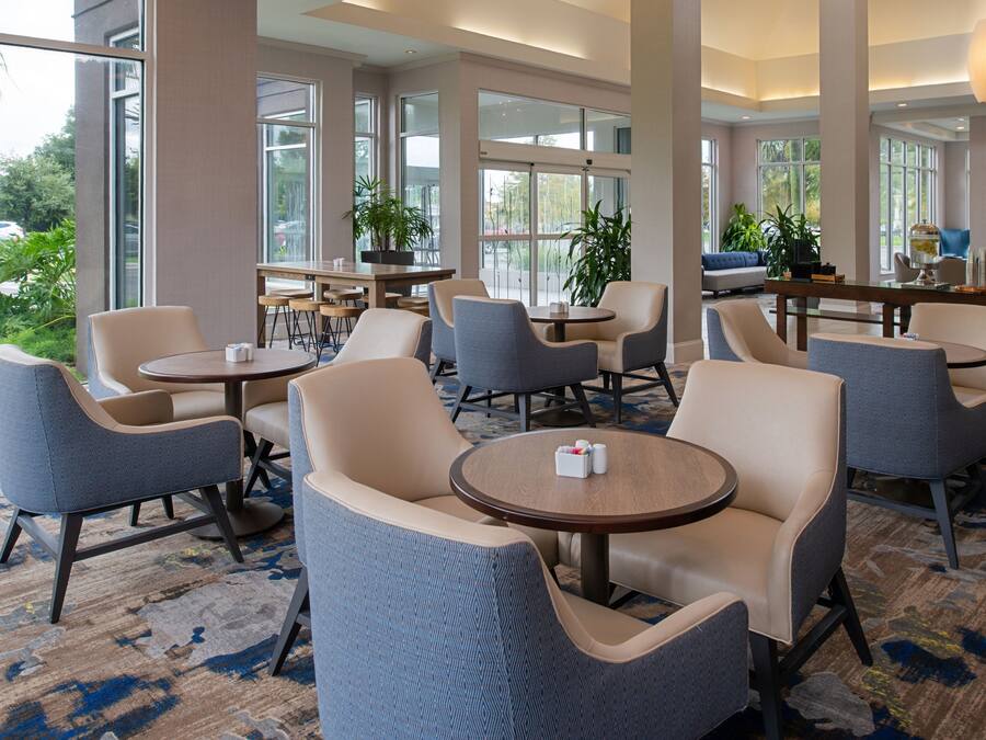 A hotel lobby with multiple seating areas, large windows, and indoor plants.
