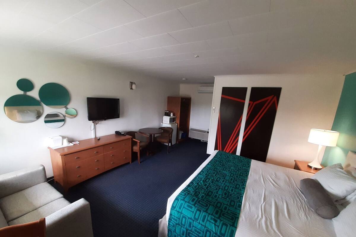A hotel room with a bed, a desk, a chair, a dresser, a television, and a microwave.