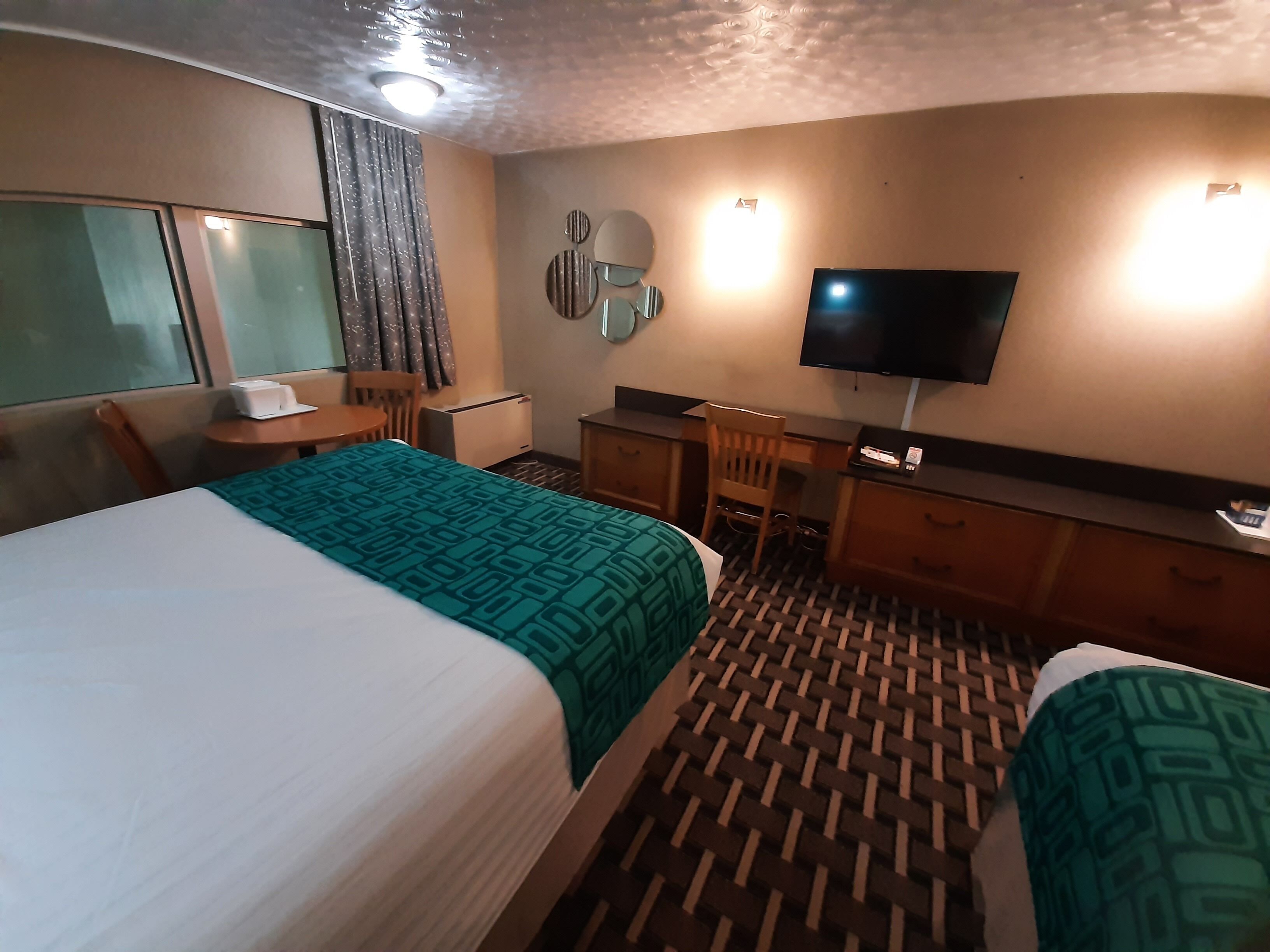 A hotel room with a bed, a desk, a chair, a television, and a window with curtains.