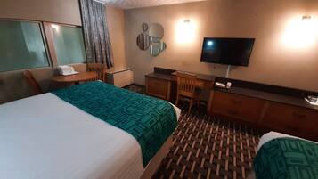 A hotel room with a bed, a desk, a chair, a television, and a window with curtains.