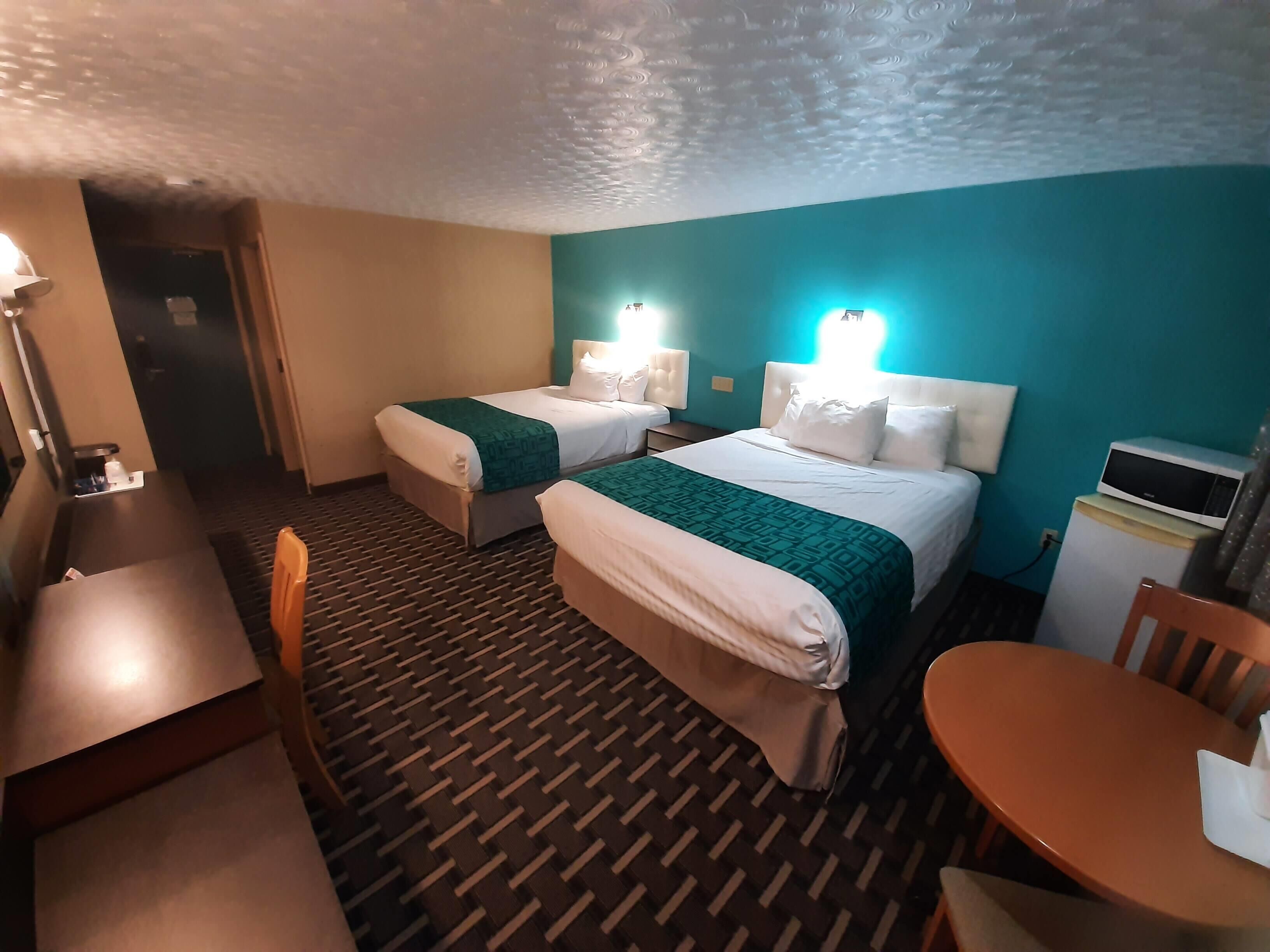 A hotel room with two beds, a desk, a chair, a microwave, and a small table.