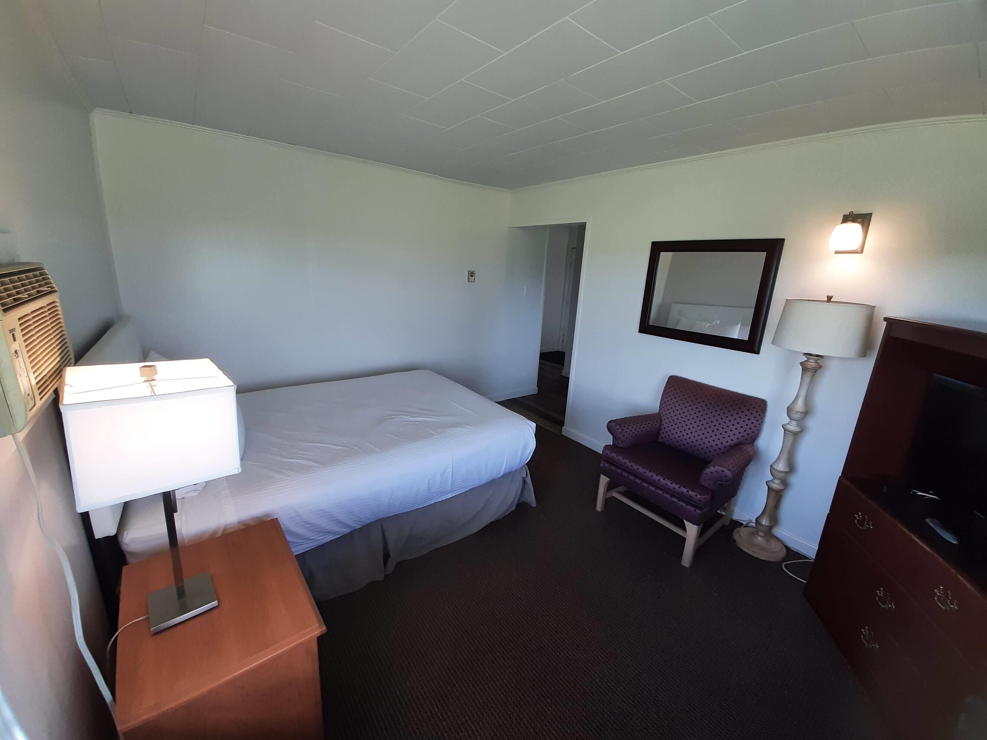 Une chambre d’hôtel comprenant un lit, une chaise, un bureau avec une lampe, une commode et un téléviseur.