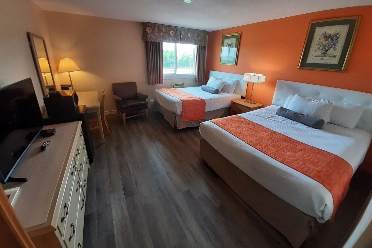 Ein Hotelzimmer mit zwei Betten, einem Fernseher, einem Schreibtisch und einem Sessel.