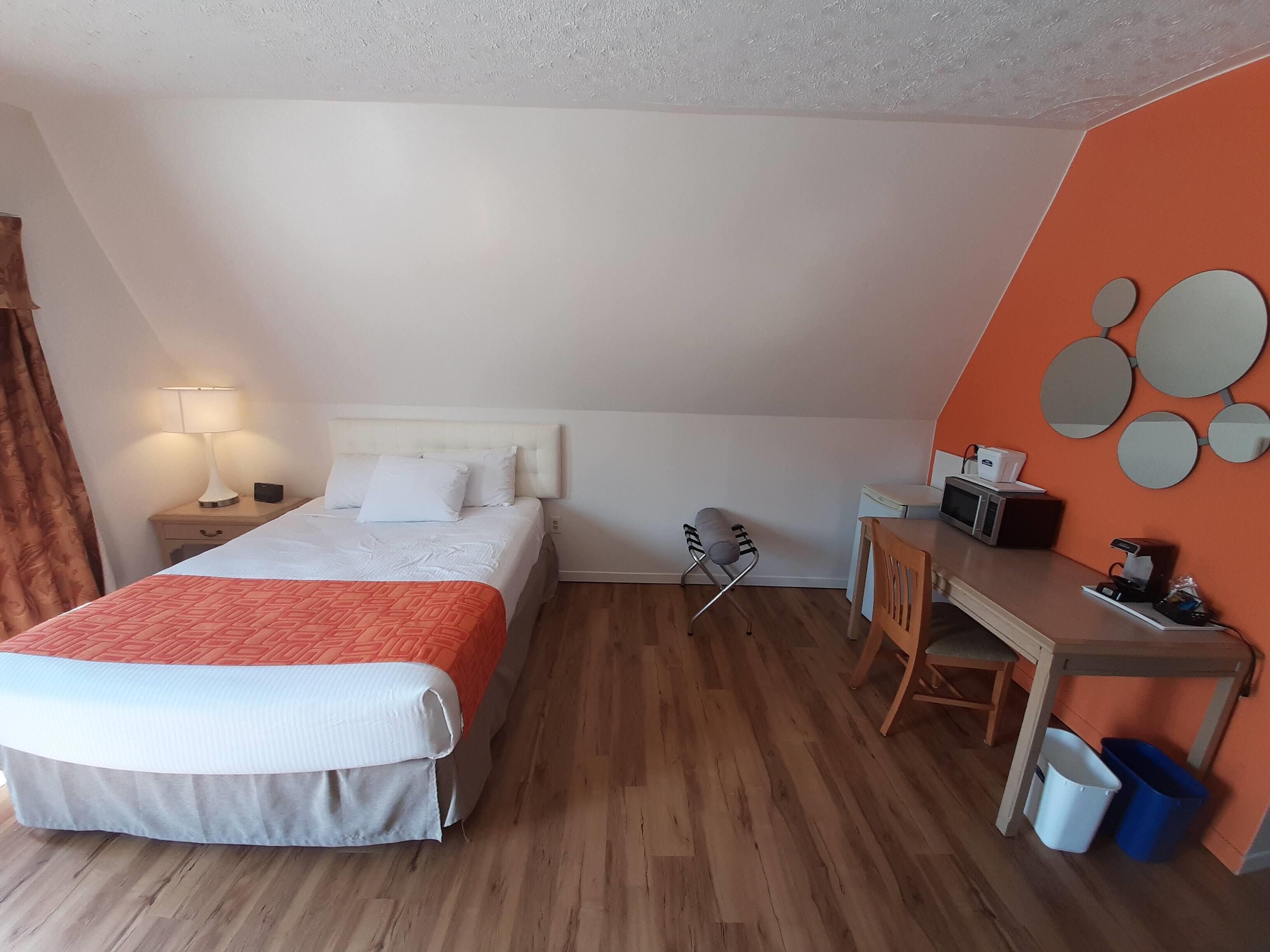 Een hotelkamer met een bed, bureau, stoel, lamp en een magnetron.