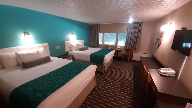 A hotel room with two beds, a desk, a chair, a television, and a window with curtains. - Howard Johnson by Wyndham Woodstock NB (Woodstock)