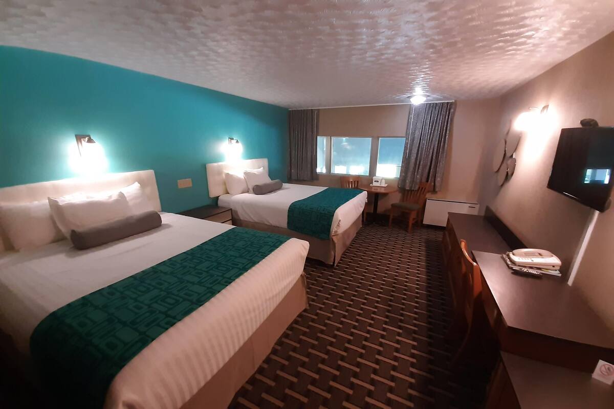 A hotel room with two beds, a desk, a chair, a television, and a window with curtains.