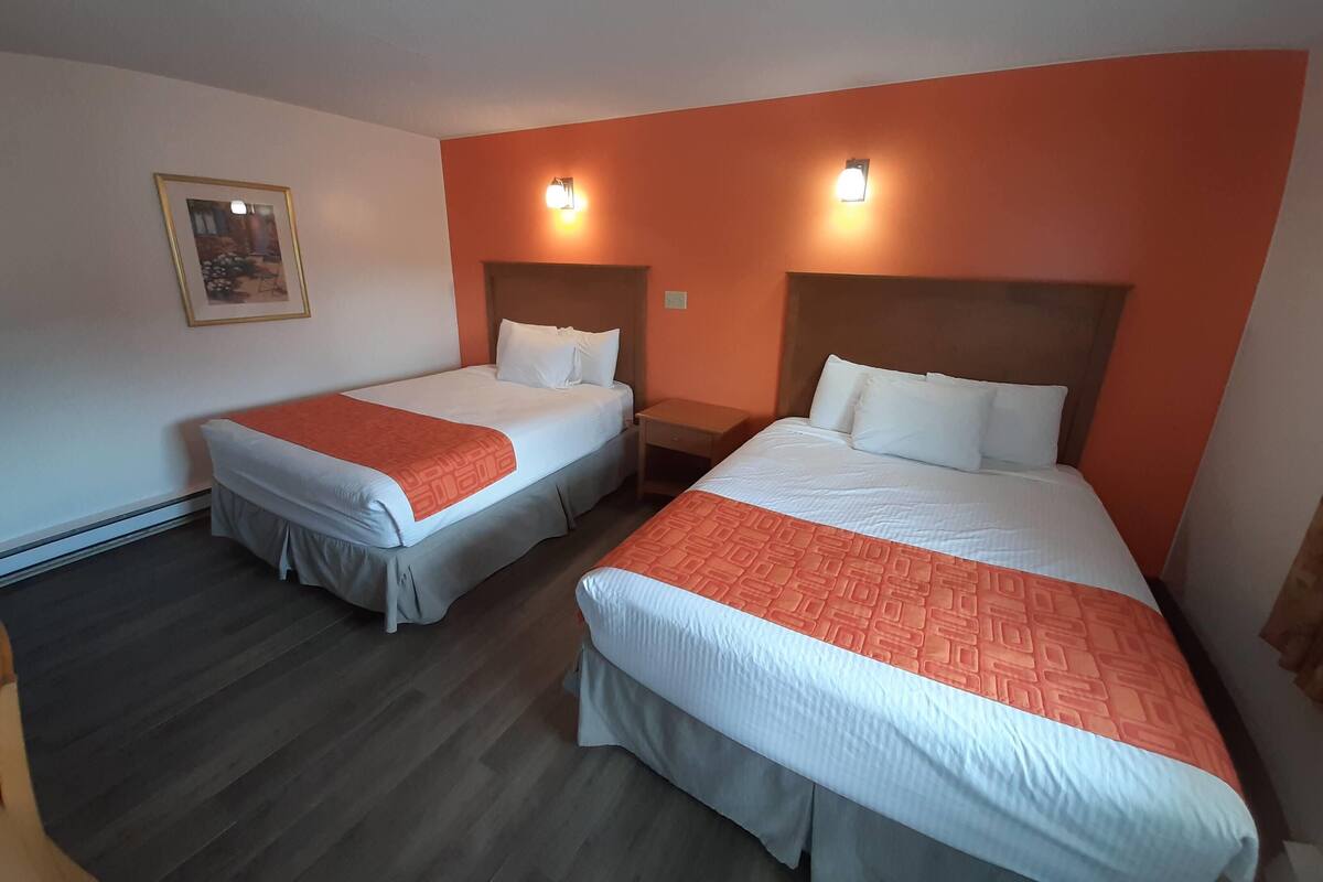A hotel room with two single beds, each with a white and orange bedspread, a wooden headboard, and a nightstand with a lamp.