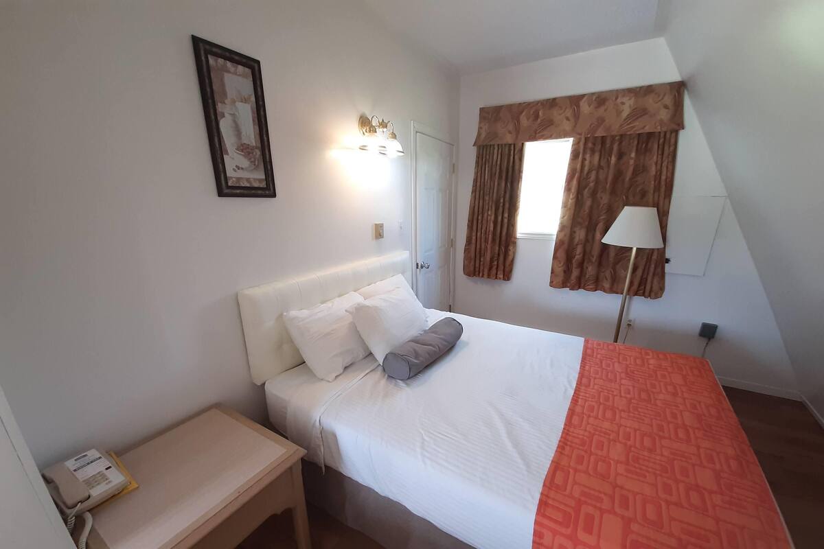A bedroom with a bed, bedside table, lamp, and a window with curtains.