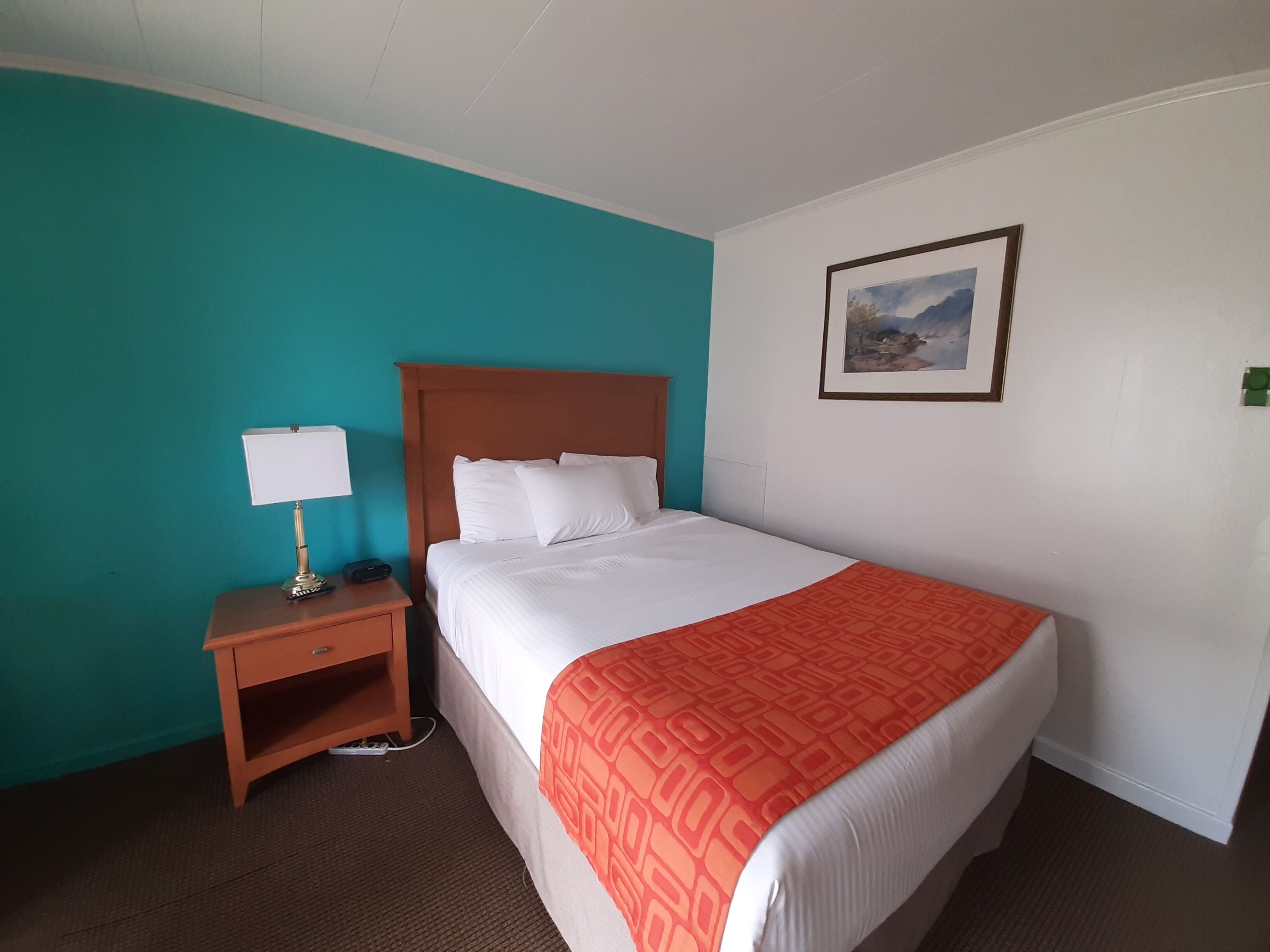 A hotel room with a bed, a nightstand with a lamp, and a painting on the wall.