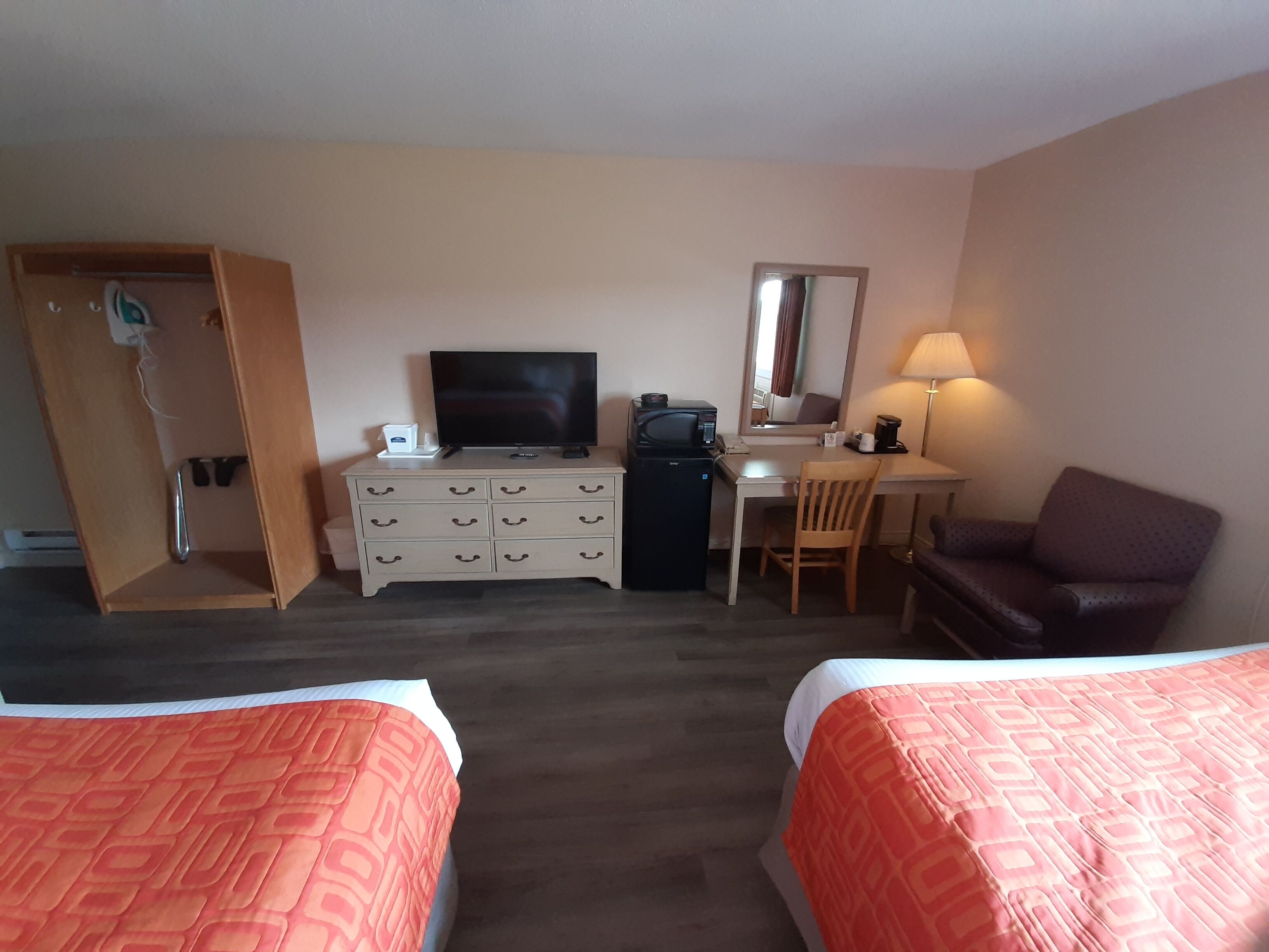 Een hotelkamer met twee bedden, een bureau met computer, een televisie, een lamp en een stoel.