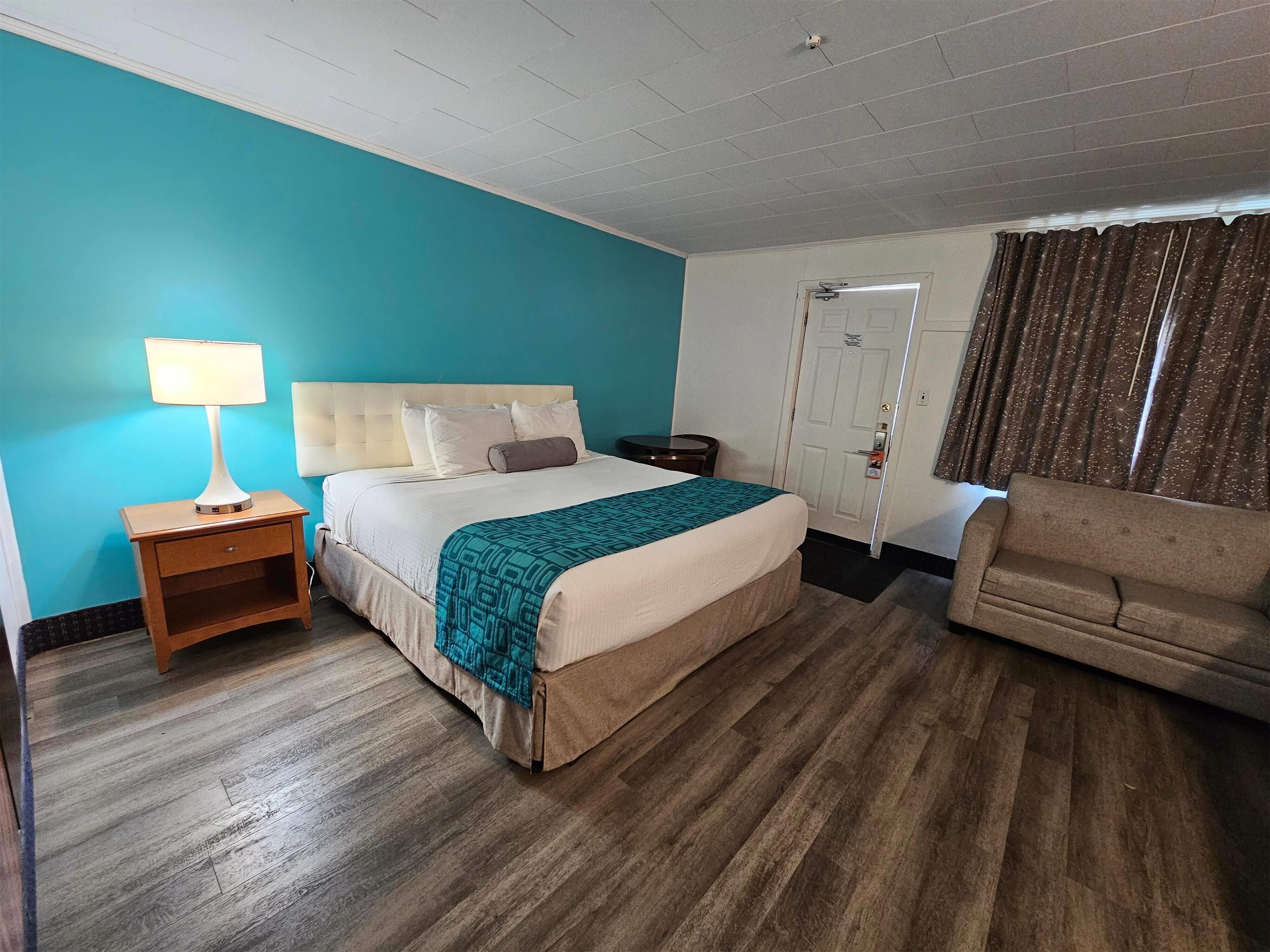 A hotel room with a bed, a nightstand, a sofa, and a door.