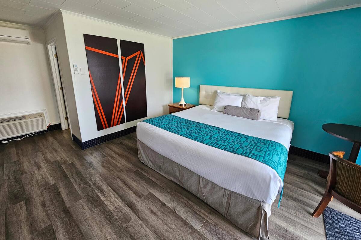 A hotel room with a bed, a nightstand, a lamp, a chair, and a wall with a geometric design.