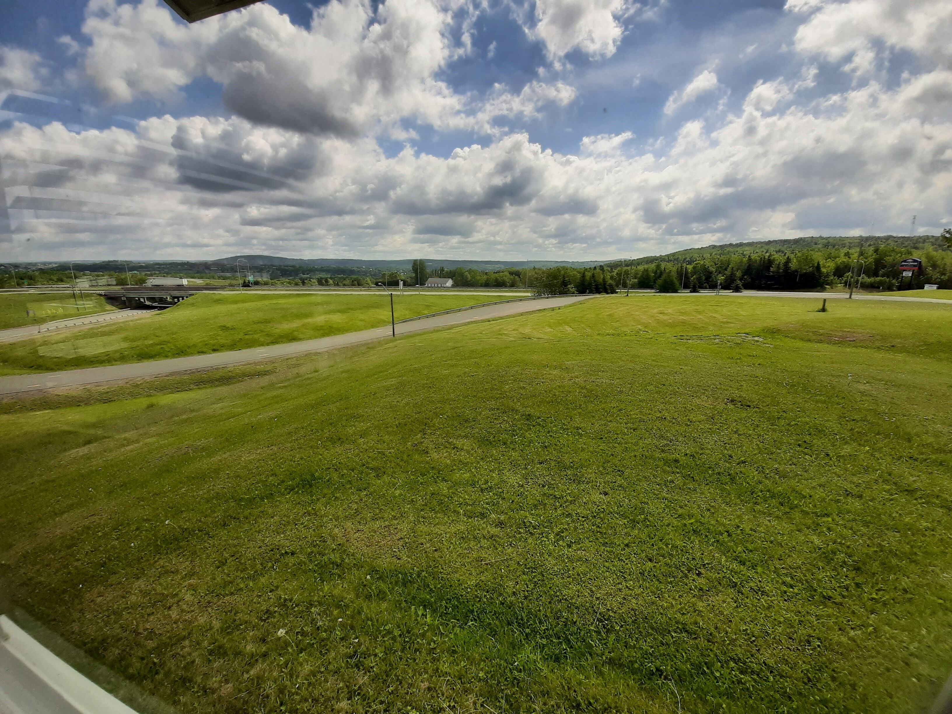 A grassy field with a road and a bridge in the background.