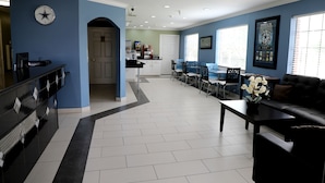 A hotel lobby with a reception desk, seating area, and a kitchenette in the background.