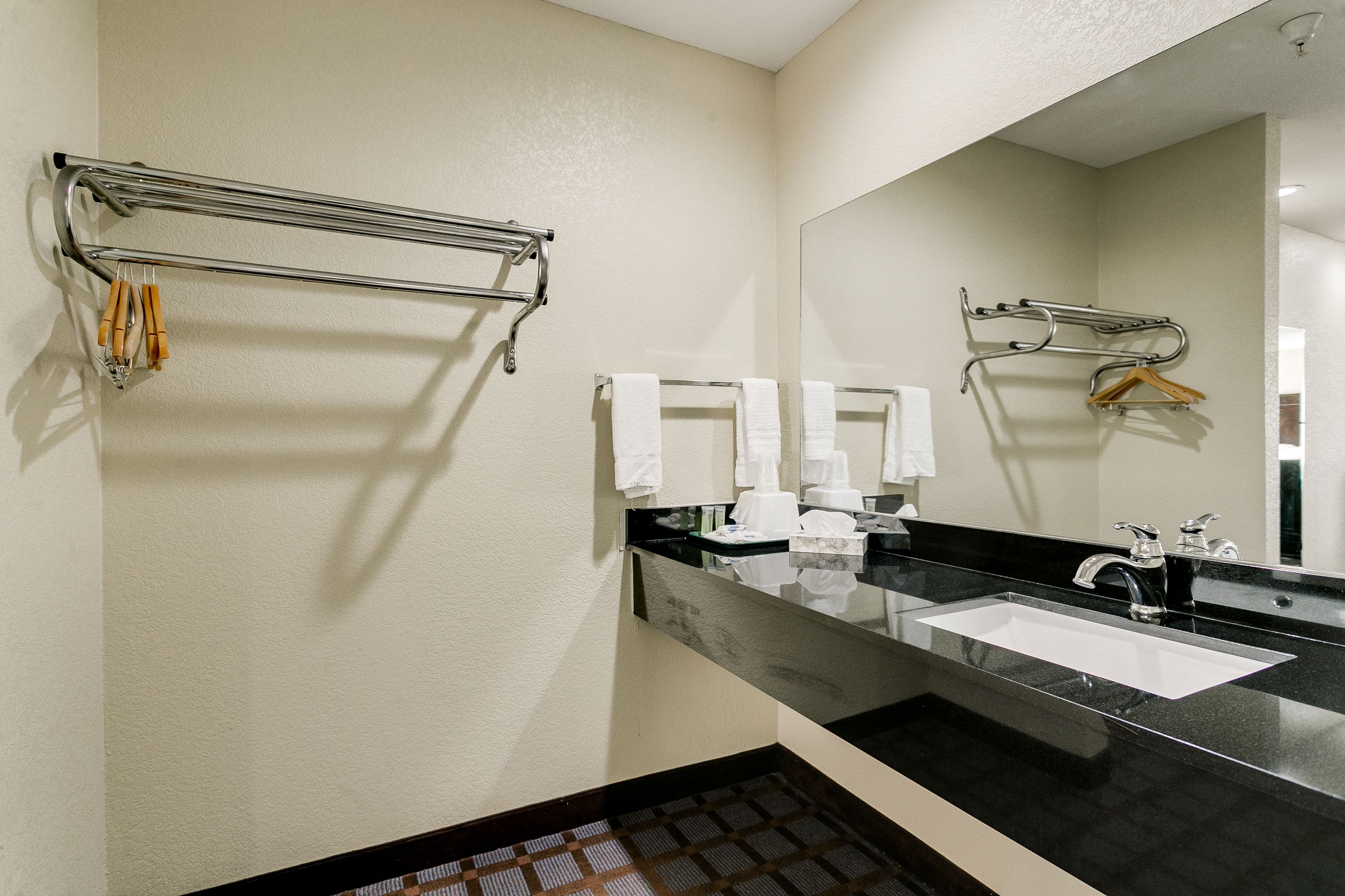 A modern bathroom with a black countertop, white sink, and two towel racks.