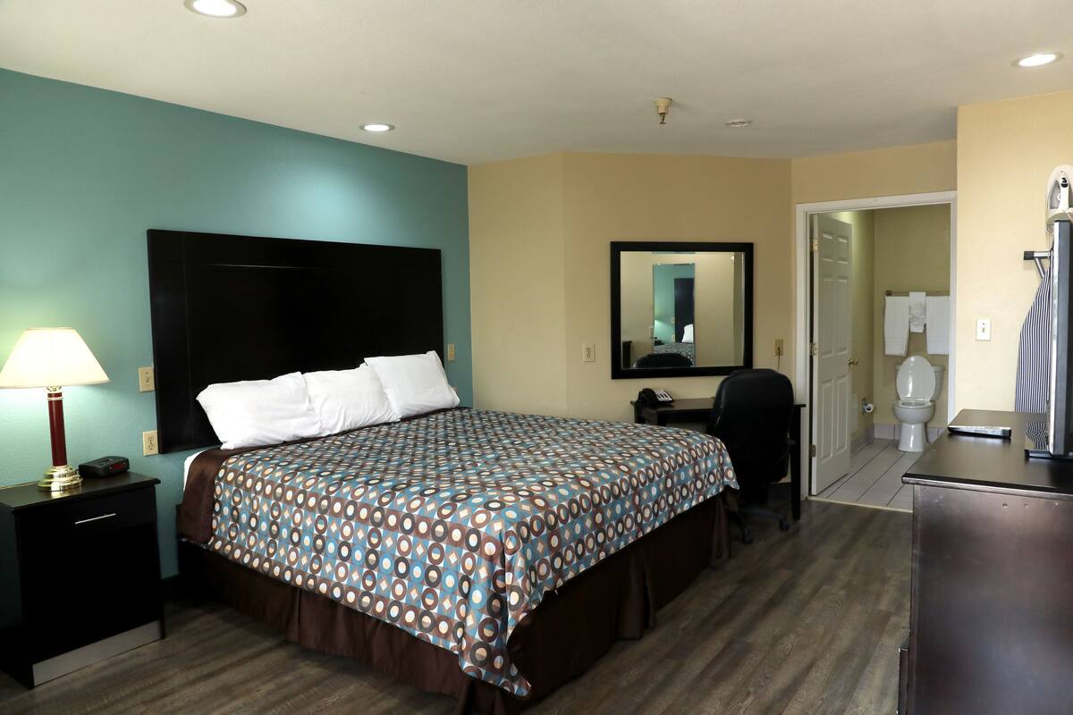 A hotel room with a bed, bedside table, lamp, and a mirror on the wall.
