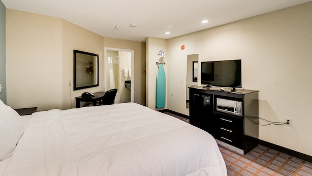 A hotel room with a large bed, a TV, a microwave, and a mirror.