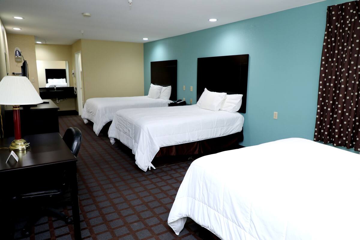 A hotel room with two beds, a desk with a lamp, a mirror, and a bathroom area.