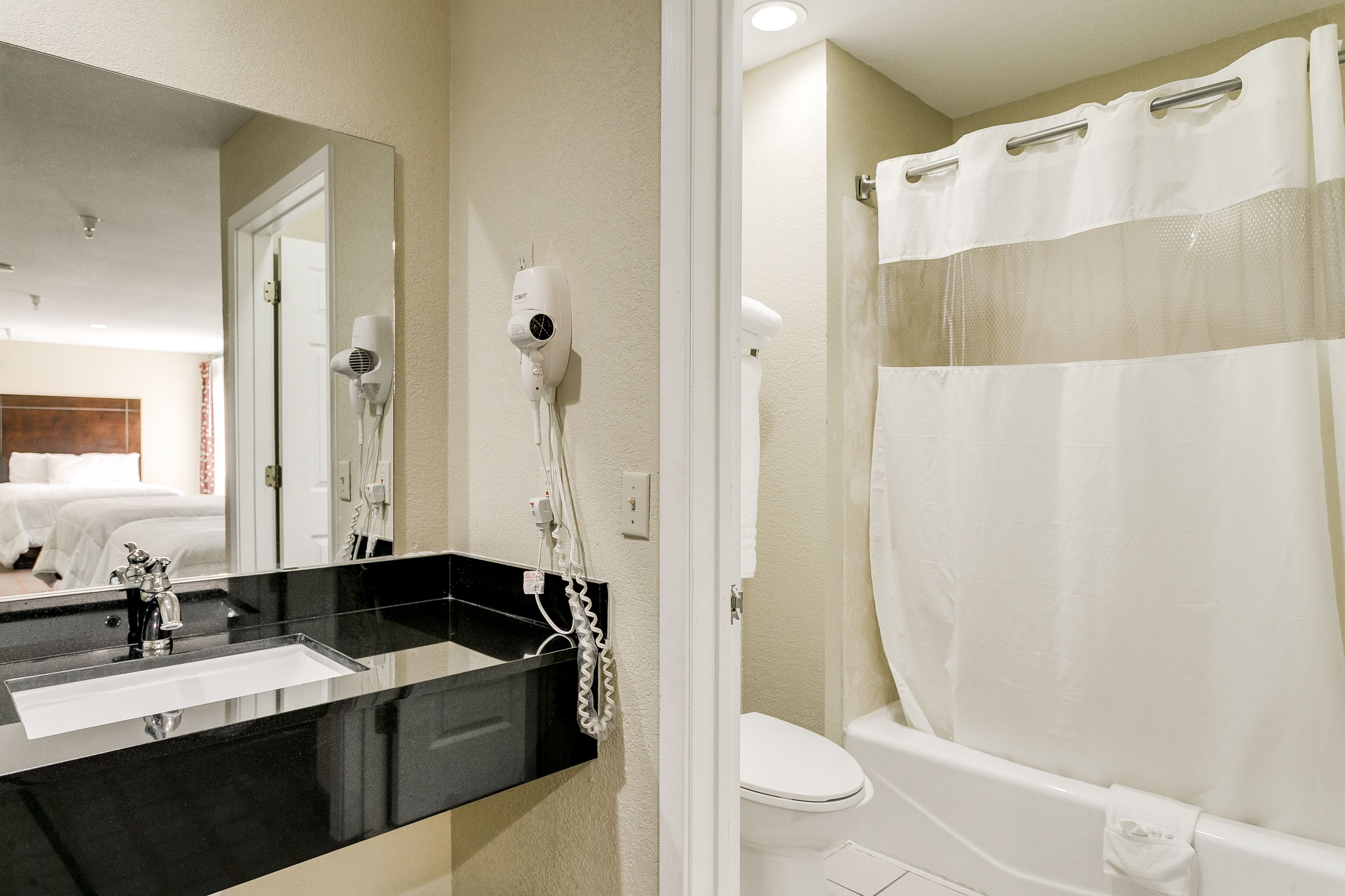 A bathroom with a black sink, a mirror, a hairdryer, a shower curtain, and a toilet.