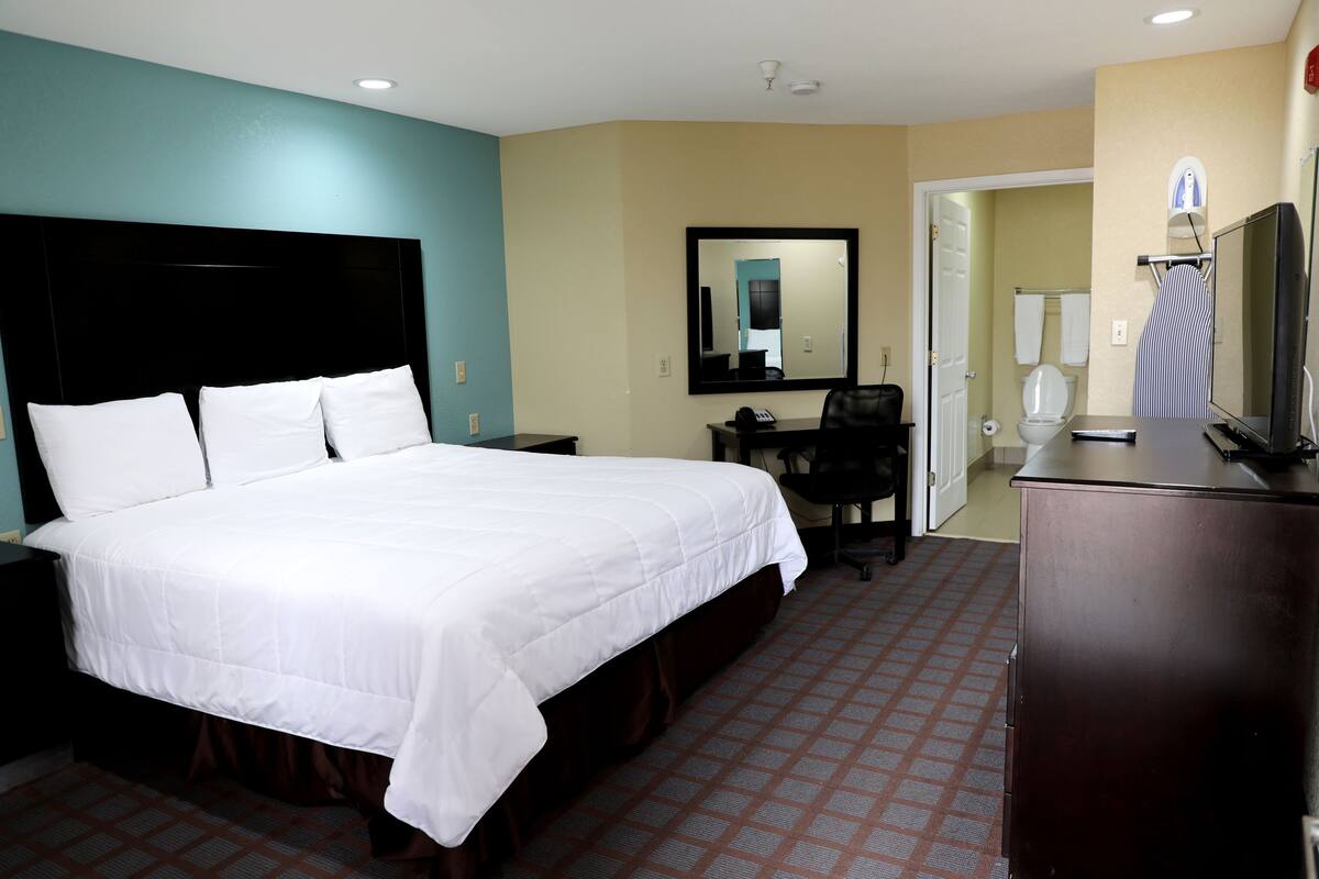 A hotel room with a large bed, a desk, a chair, a television, and a bathroom visible through an open door.