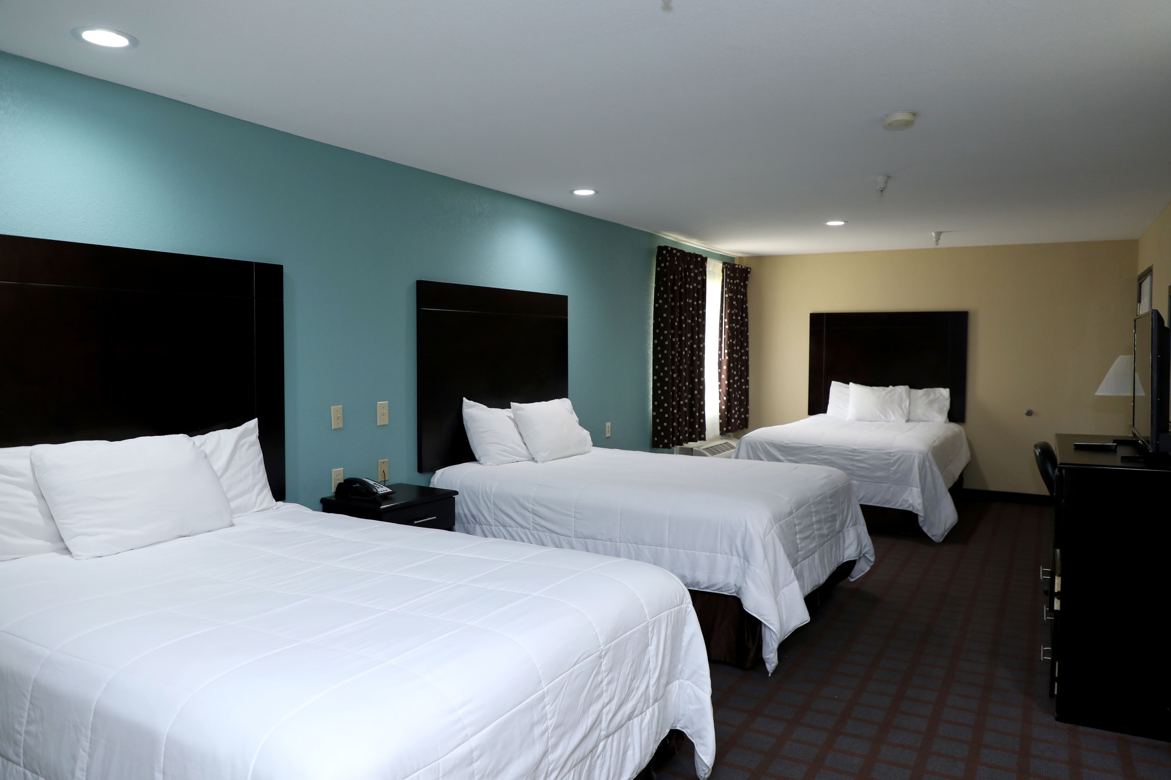 A hotel room with three single beds, a desk, a chair, and a TV.