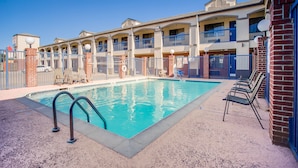 A hotel with a swimming pool, outdoor seating, and a brick facade.