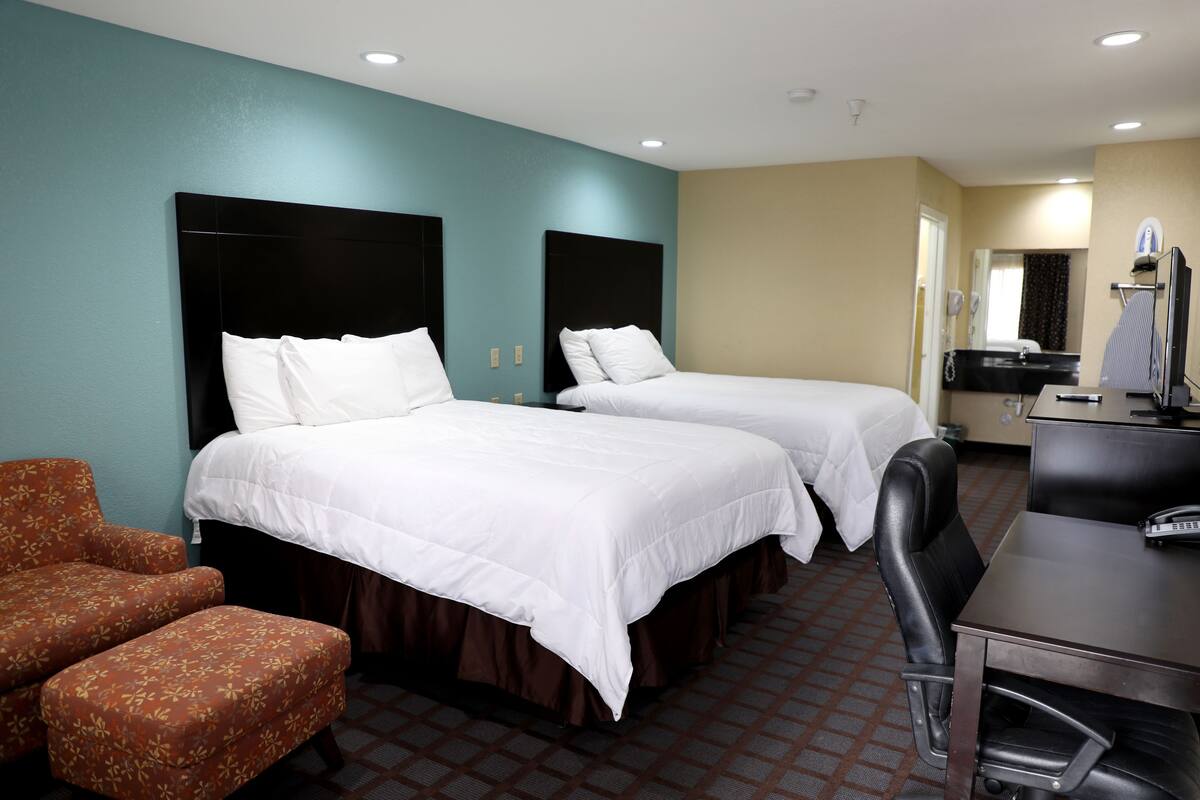 A hotel room with two beds, a desk, a chair, and a TV.
