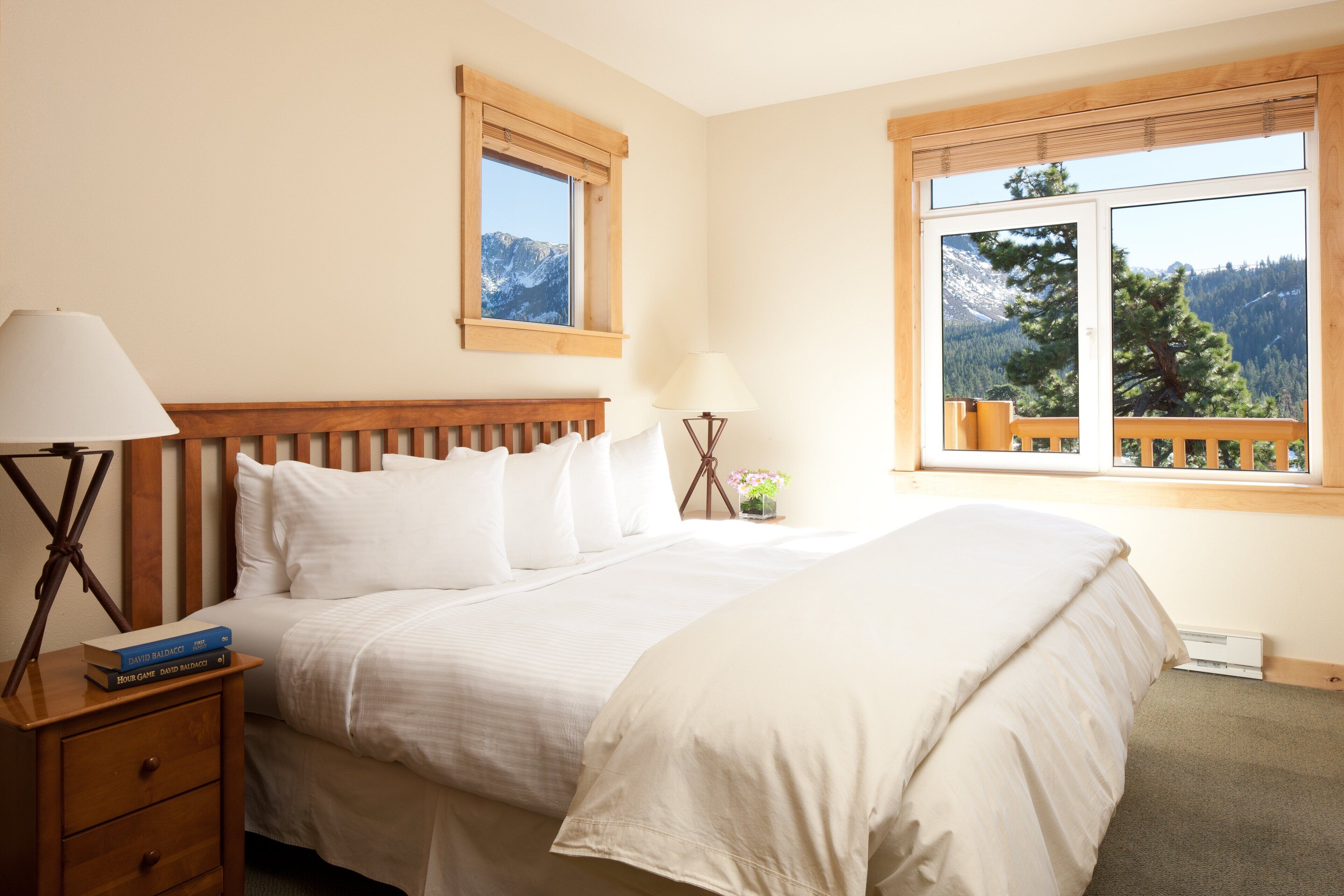Un dormitorio con una cama grande, dos mesitas de noche, una mesita auxiliar, un ventanal con vistas a la montaña y un cabecero de madera.