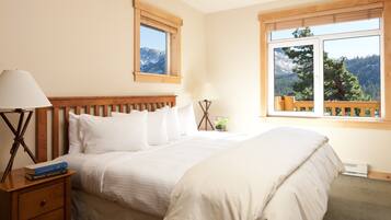 A bedroom with a large bed, two bedside tables, a nightstand, a window with a mountain view, and a wooden headboard.