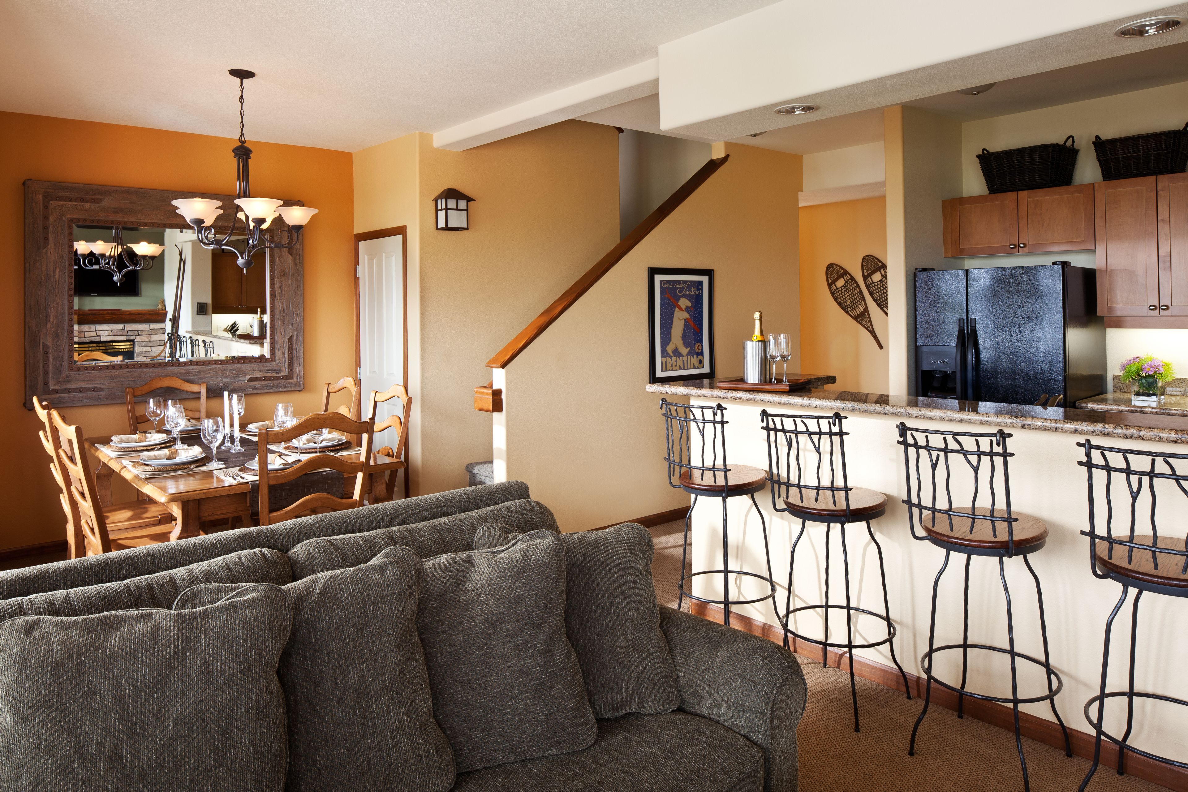 A modern kitchen with a large island, bar stools, and a dining area with a sofa and table set for dining.