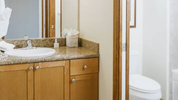 A bathroom with a wooden vanity, a sink, a mirror, and a toilet.