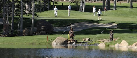 Golfkenttä, jossa on lampi, puita ja karhupatsas.