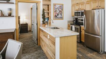 A modern kitchen with wooden cabinets, a stainless steel refrigerator, a microwave, and a sink.