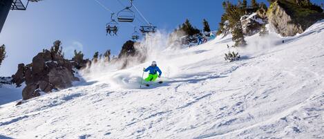 A ski slope with a person skiing down, ski lift chairs, and rocky terrain.