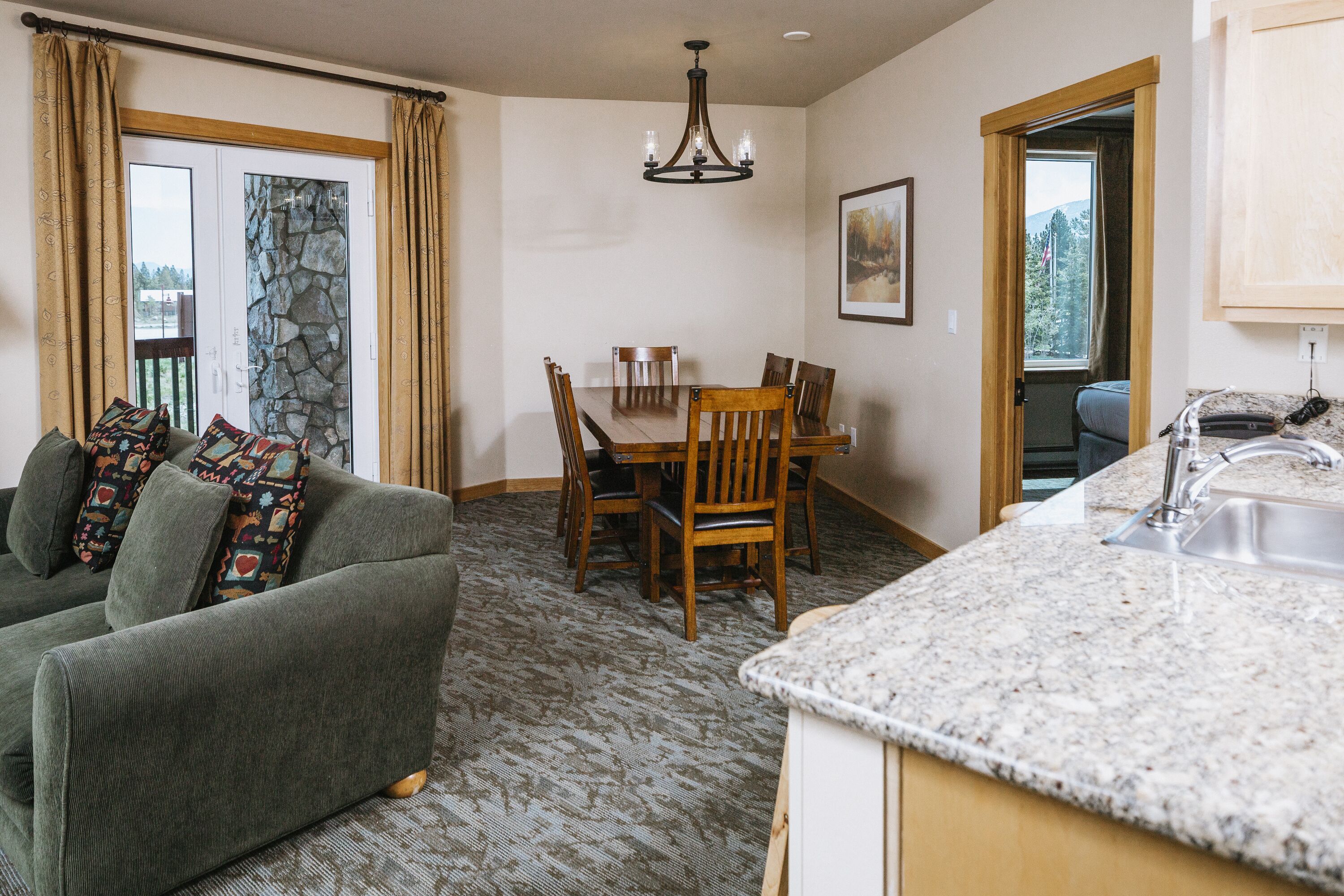 A cozy living room with a green sofa, a dining table with chairs, a kitchen area with granite countertops, and a stone wall.