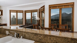A kitchen with granite countertops, a white sink, wooden chairs, and large windows with a mountain view. - Juniper Springs Resort (Mammoth Lakes)