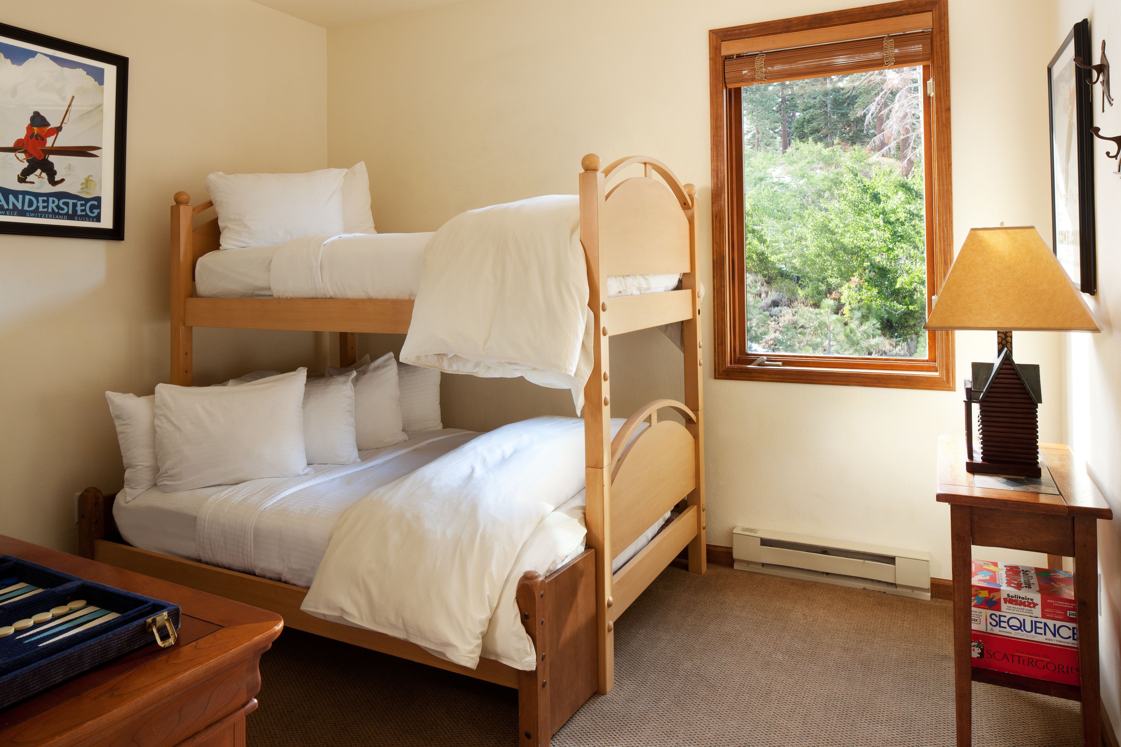 A bunk bed room with a window, a desk with a lamp, and a framed picture on the wall.